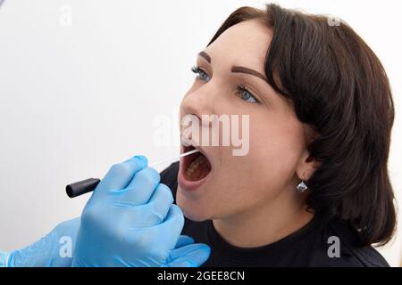 Medico in tuta protettiva che prende una gola e un tampone nasale da un paziente per verificare la possibile infezione da coronavirus o covid Foto Stock