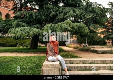 Foto d'inventario di una donna musulmana seduta su un muro. Indossa un Hiyab Foto Stock