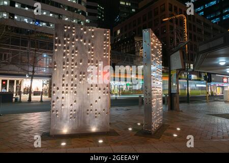 Wellington Nuova Zelanda - Luglio 29 2021; Notte in città a livello di strada edifici a lunga esposizione dietro sculture di arte pubblica in acciaio inossidabile chiamato Invis Foto Stock