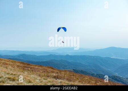 Parapendio sulle montagne con paracadute. Parapendio dietro le colline blu cielo gamma paesaggio. Le persone attive di sport turistici volano utilizzando Parachute. Foto Stock