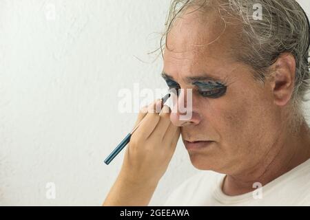 mano di una ragazza che dipinge gli occhi di un uomo maturo serio con cosmetico su sfondo bianco Foto Stock