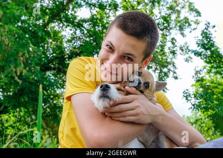 L'uomo abbraccia due cani e sorride allegramente nel parco Foto Stock