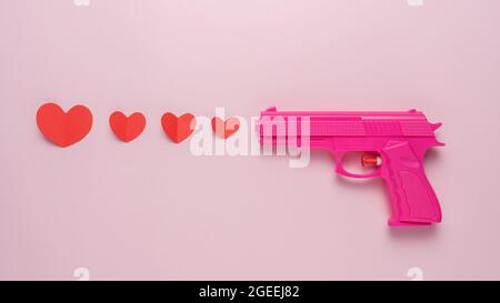 Sfondo creativo realizzato con pistola rosa e cuori di carta rossa. Concetto di amore minimo. Foto Stock
