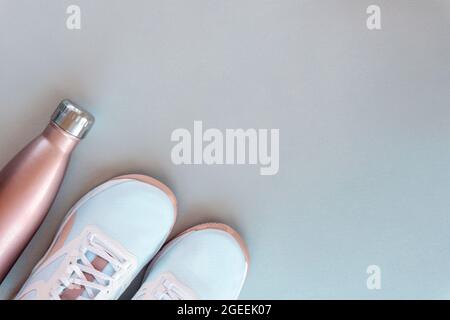 Sneaker bianche e bottiglia con acqua su sfondo grigio neutro. Concetto di vita sana, sport e formazione. Vista dall'alto, disposizione piatta, spazio di copia Foto Stock