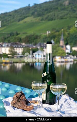 Vino riesling di qualità bianca in bottiglia verde servito sul vecchio ponte sul fiume Mosel con vista sulla città vecchia tedesca in giornata di sole Foto Stock