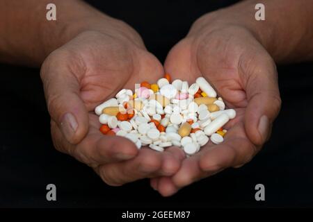 Una manciata di varie pillole in mani maschili su sfondo nero Foto Stock