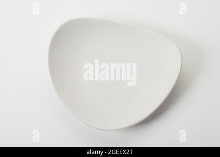 New small rounded triangle-shaped white ceramic dessert plate on white background Foto Stock