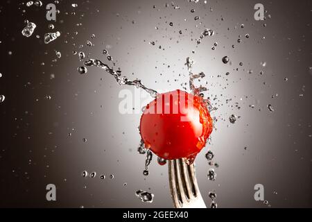 ciliegia di pomodoro su una forchetta in spruzzi d'acqua. Sfondo bianco nero Foto Stock