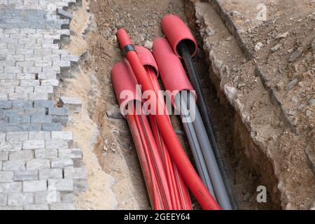 Un gran numero di cavi elettrici e di rete Internet ad alta velocità in tubo rosso corrugato sono sepolti sotterranei sulla strada coperta di ciottoli Foto Stock