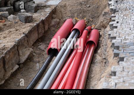 Un gran numero di cavi elettrici e di rete Internet ad alta velocità in tubo rosso corrugato sono sepolti sotterranei sulla strada coperta di ciottoli Foto Stock