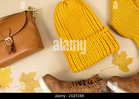 Borsa donna in pelle arancione, maglione a maglia, cappello, foglie autunnali su sfondo beige. Accessori alla moda per l'autunno. Abbigliamento accogliente Foto Stock