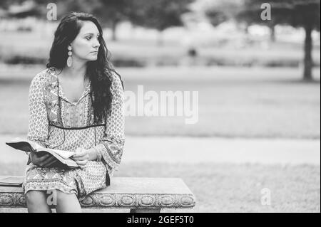 Giovane donna caucasica che legge la Bibbia mentre si siede su una panchina Foto Stock