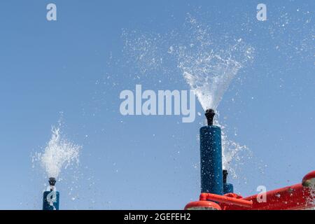Due spruzzatori blu del parco acquatico spruzzano l'acqua nel cielo per il divertimento estivo dei bambini. Foto Stock