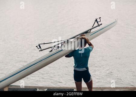 Sportivo single scull man vogatore che porta barca a concorrenza su acqua di lago Foto Stock