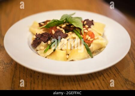 Jerusalem carciofo crema pappardelle: Un pasto vegano con pasta, pomodori ciliegini arrosto, olive spalmate, asparagi, pinoli e basilico su un piatto Foto Stock