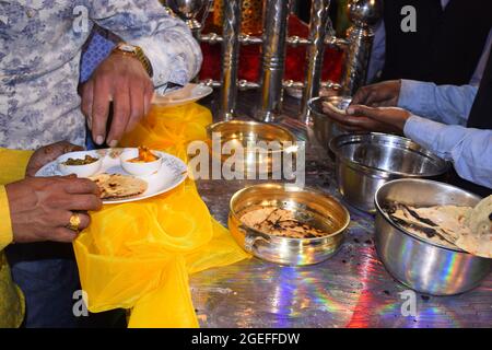 Mano di uomo indiano che porta Tandoori Roti nel suo piatto da una pentola grande Foto Stock