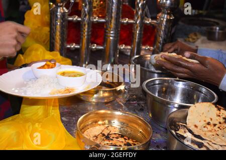 Mano di uomo indiano che porta Tandoori Roti nel suo piatto da una pentola grande Foto Stock