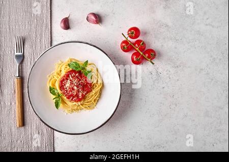 Pasta con pomodoro, parmigiano, aglio e basilico su piatto bianco con forchetta e tovagliolo su sfondo chiaro. Disposizione piatta, spazio di copia Foto Stock