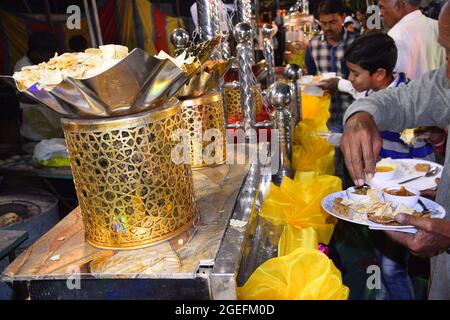 Uomo indiano che porta papad nel suo piatto da un vaso grande luminoso nella cerimonia di nozze Foto Stock