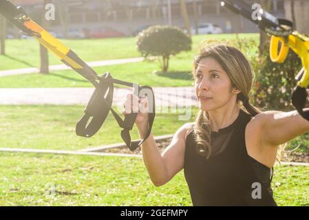 Fitness donna che si esercita con fitness cinghie nel parco Foto Stock