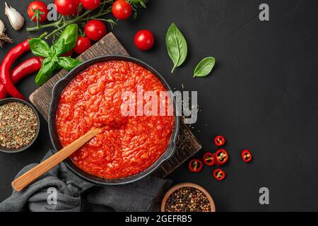 Salsa di pomodoro italiana di base con basilico e pepe su sfondo nero con ingredienti. Salsa Marinara. Vista dall'alto, spazio di copia. Foto Stock