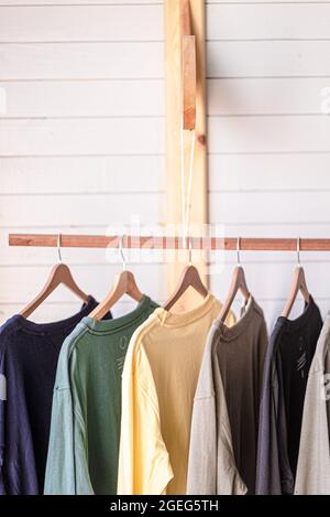 Vista di un paio di t-shirt colorate con appendiabiti appesi sul palo di legno in camera Foto Stock