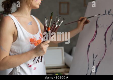 Primo piano delle mani di un artista donna che tiene un sacco di pennelli e vernici su carta. Foto Stock