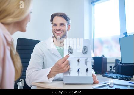Medico amichevole che offre diversi sussidi sordi al suo un paziente Foto Stock