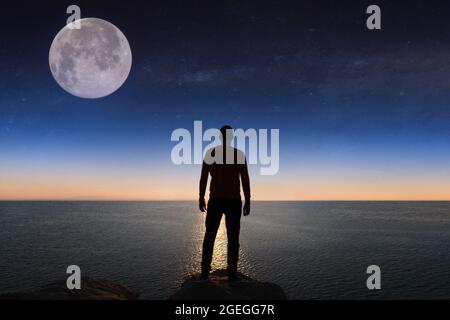 Silhouette di uomo è guardare il tramonto sul mare e scogliere. Foto Stock