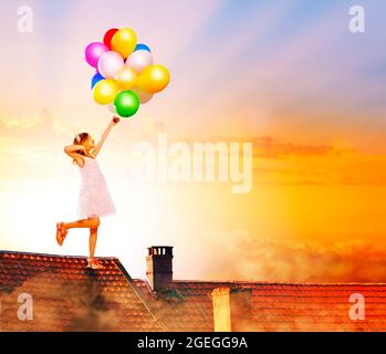 Piccola ragazza saltare con palloncini sul tetto della casa Foto Stock