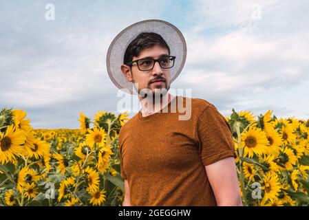 Giovane uomo con cappello e bicchieri in un campo di girasoli Foto Stock