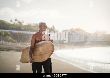 Uomo anziano che si diverte a surfing durante il tramonto - Fit allenamenti in pensione con tavole da surf sulla spiaggia Foto Stock