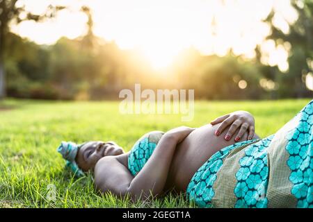 Giovane donna incinta africana sdraiata sul parco verde erba durante il tramonto - concetto di stile di vita di maternità Foto Stock