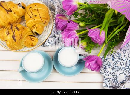 Tre croissant, due tazze di caffè sul tavolo e un mazzo di bellissimi tulipani-close-up. Foto Stock