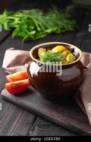 Patate, pollo e zucchine cotte in una pentola di argilla su sfondo scuro. Foto Stock