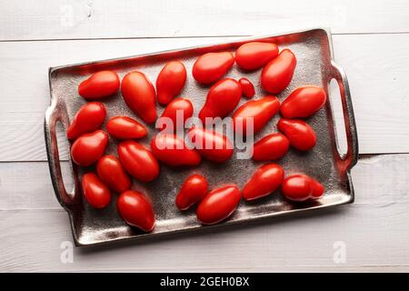 Succosa pomodori a forma di fragola rosso brillante su un vassoio di metallo, primo piano, su un tavolo di legno, vista dall'alto. Foto Stock