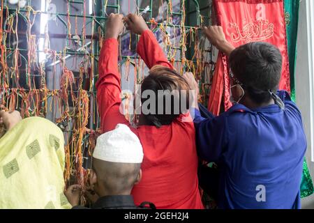 Dhaka, Bangladesh. 20 ago 2021. I musulmani del Bangladesh Shia legano i fili colorati ad una recinzione.Ashura è il decimo giorno di Muharram, il primo mese del calendario islamico, osservato in tutto il mondo in ricordo del martirio di Imam Hussain, il nipote del profeta Muhammad. Credit: SOPA Images Limited/Alamy Live News Foto Stock