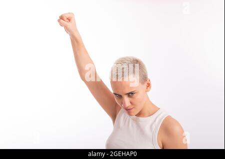 Giovane donna caucasica che tiene il pugno su uno sfondo bianco. Una ragazza con capelli corti sta combattendo per i diritti Foto Stock