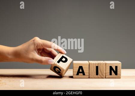 La mano femminile capovolge i cubi di legno con dolore di parola per guadagnare. CopySpace per l'annuncio. Foto Stock