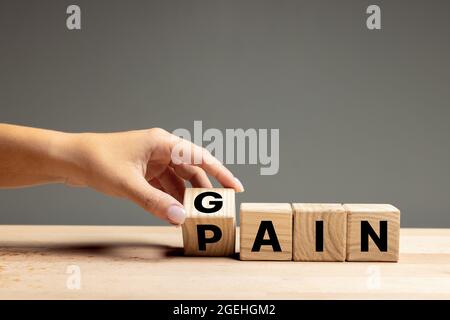 La mano femminile capovolge i cubi di legno con dolore di parola per guadagnare. CopySpace per l'annuncio. Foto Stock