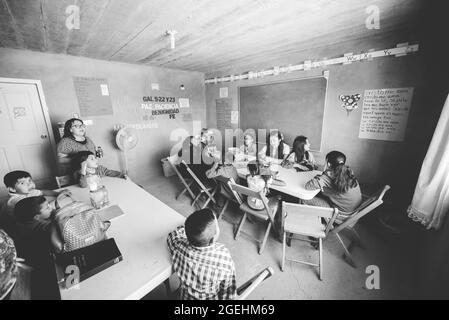 ZACATECAS, MESSICO - Apr 01, 2018: Una foto in scala di grigi di un gruppo di bambini e di un insegnante seduto da un tavolo e imparare in una piccola chiesa del villaggio messicano Foto Stock