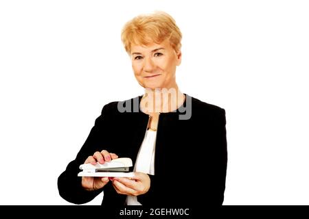 Anziana lavoratrice caucasica che tiene una graffatrice e sorride su uno sfondo bianco Foto Stock