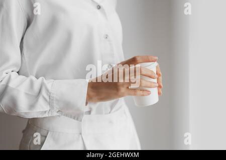 Donna irriconoscibile in camicia bianca che tiene la tazza di caffè. Foto Stock