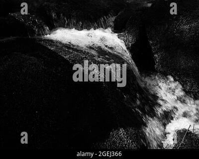 Foto in bianco e nero di un piccolo ruscello che cade sulle rocce Foto Stock