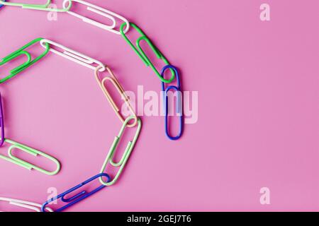 Una catena di graffette in carta multicolore su sfondo rosa. Concetto di comunicazione e cooperazione commerciale Foto Stock