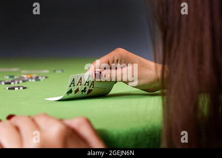 Donna che gioca a poker e guarda le carte. Tavolo verde, chip e quattro assi carte in mano. Messa a fuoco superficiale. Foto Stock