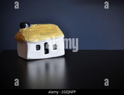 Glenshee Pottery (Scozia) - bothy in ceramica con tetto in paglia adagiato su un tavolo scuro con sfondo blu scuro. Spazio di copia rimanente intorno all'immagine Foto Stock