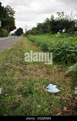 Una maschera usa e getta scartata nel verge erba lungo una strada di campagna sul bordo di un villaggio Foto Stock