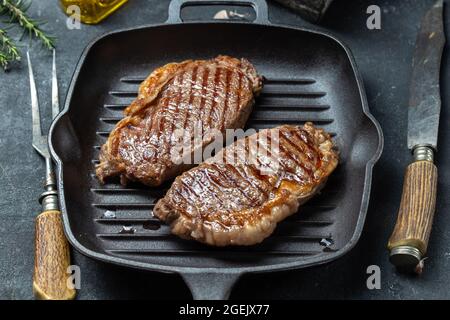 Bistecca di lombo fritta su tegame in ghisa con olio d'oliva e rosmarino, fondo nero. Foto Stock