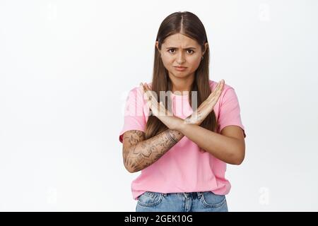 Ritratto di donna mostra segno croce, stop gesture e guardare qualcosa che lei non piace, in piedi dispiaciuto su sfondo bianco Foto Stock